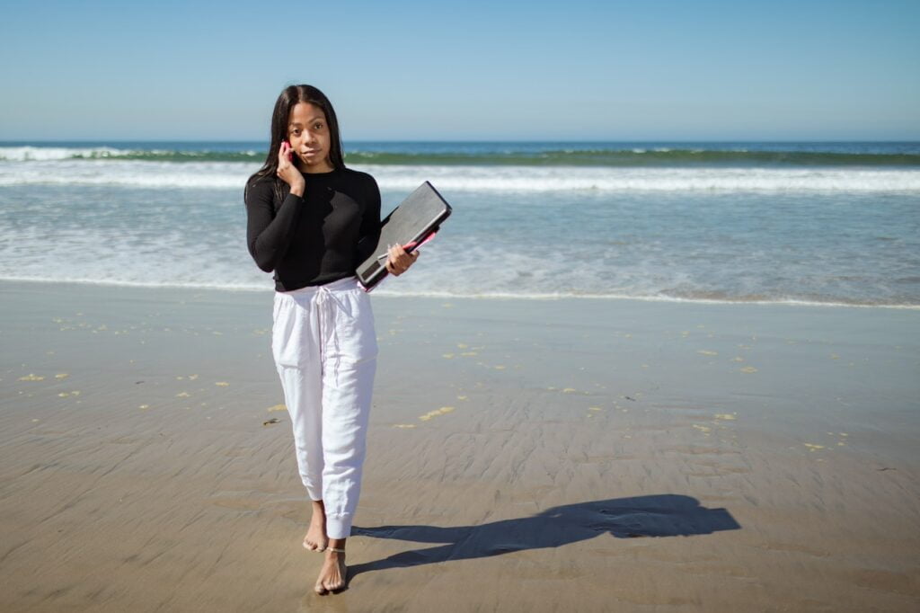 Femme marchant sur la plage tenant un livre.
